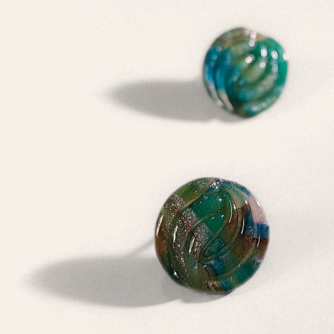 Green marbled round polymer clay studs with parallel curved ridges, angled view