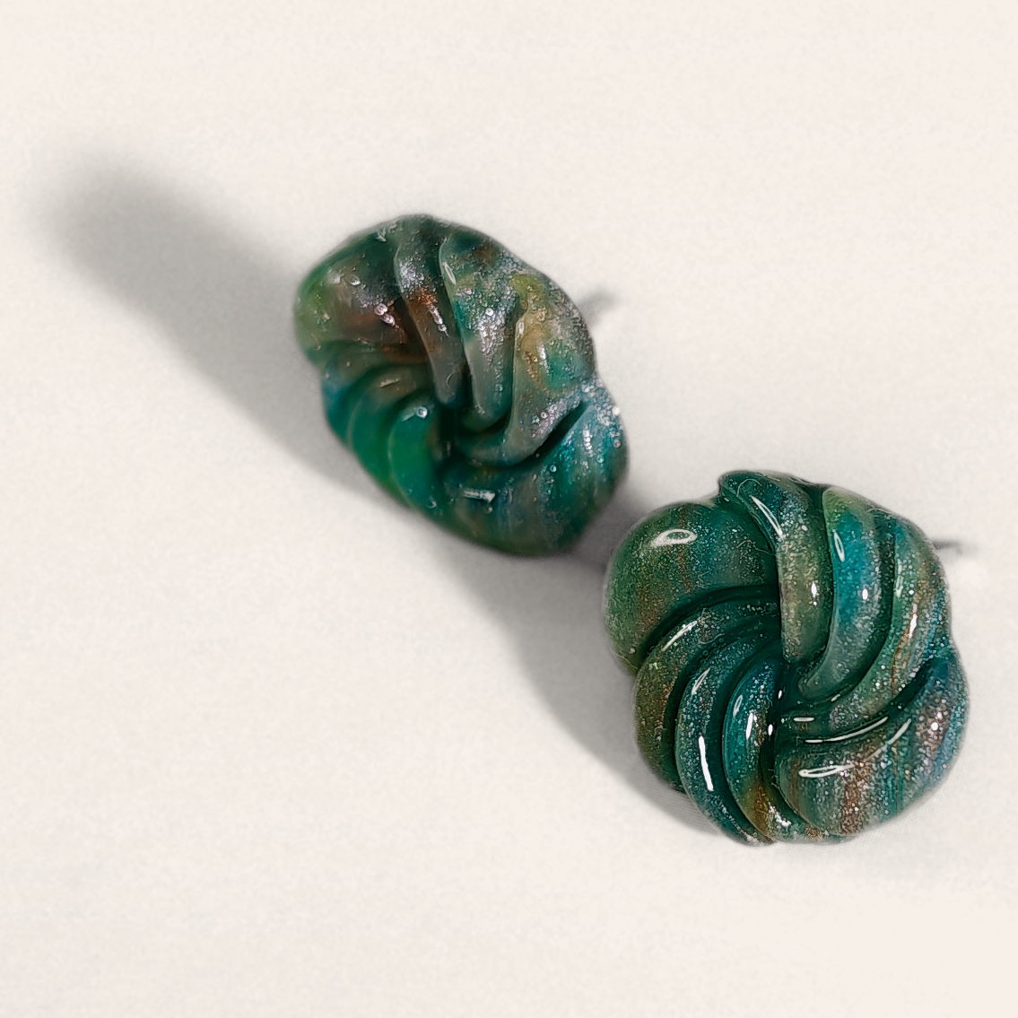 Green marbled round polymer clay studs with spiral ridges, angled view